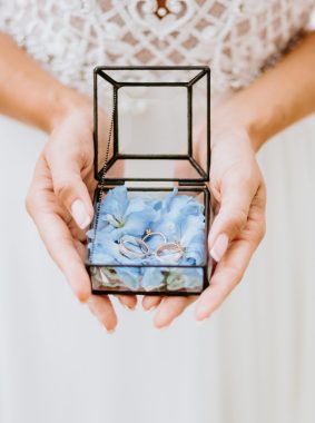 bride holding wedding ring box. glass box with weddding ring in petals.